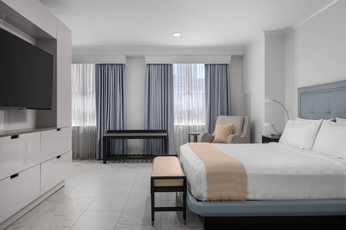 A modern hotel room with a large bed, a TV, a desk, and a chair.