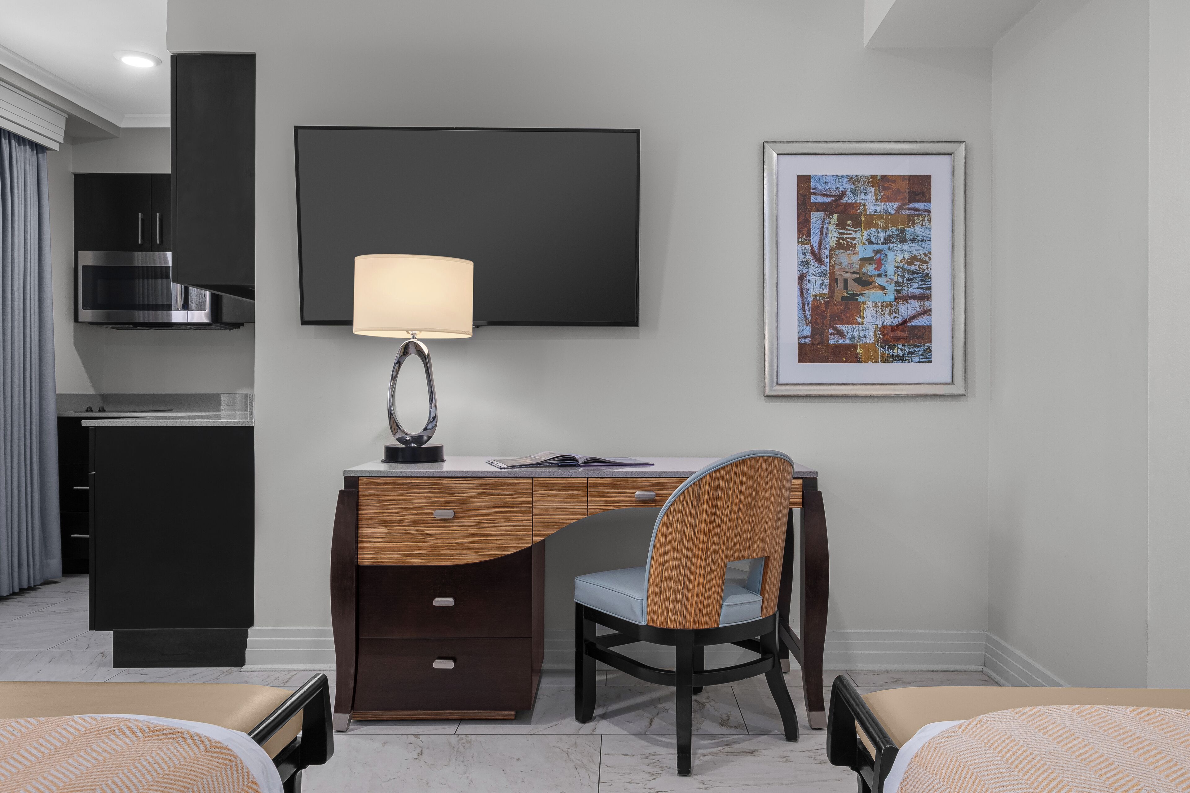 Una habitación de hotel moderna con escritorio, silla, cama, televisión y obras de arte.