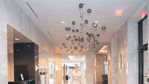 Un hall d’entrée spacieux, agrémenté d’un lustre moderne, d’un comptoir de réception et d’une signalétique claire indiquant les sorties.