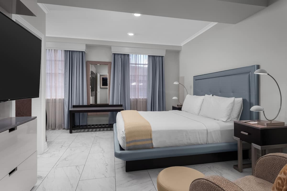 A modern hotel room with a large bed, a desk, a TV, and a mirror.