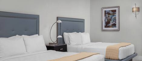 A hotel room with two beds, a nightstand with a lamp, a framed picture on the wall, and a modern light fixture.
