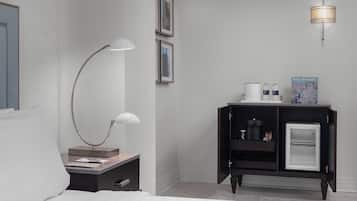 A hotel room with a bed, a desk with a lamp, a minibar, and a wall-mounted light fixture.