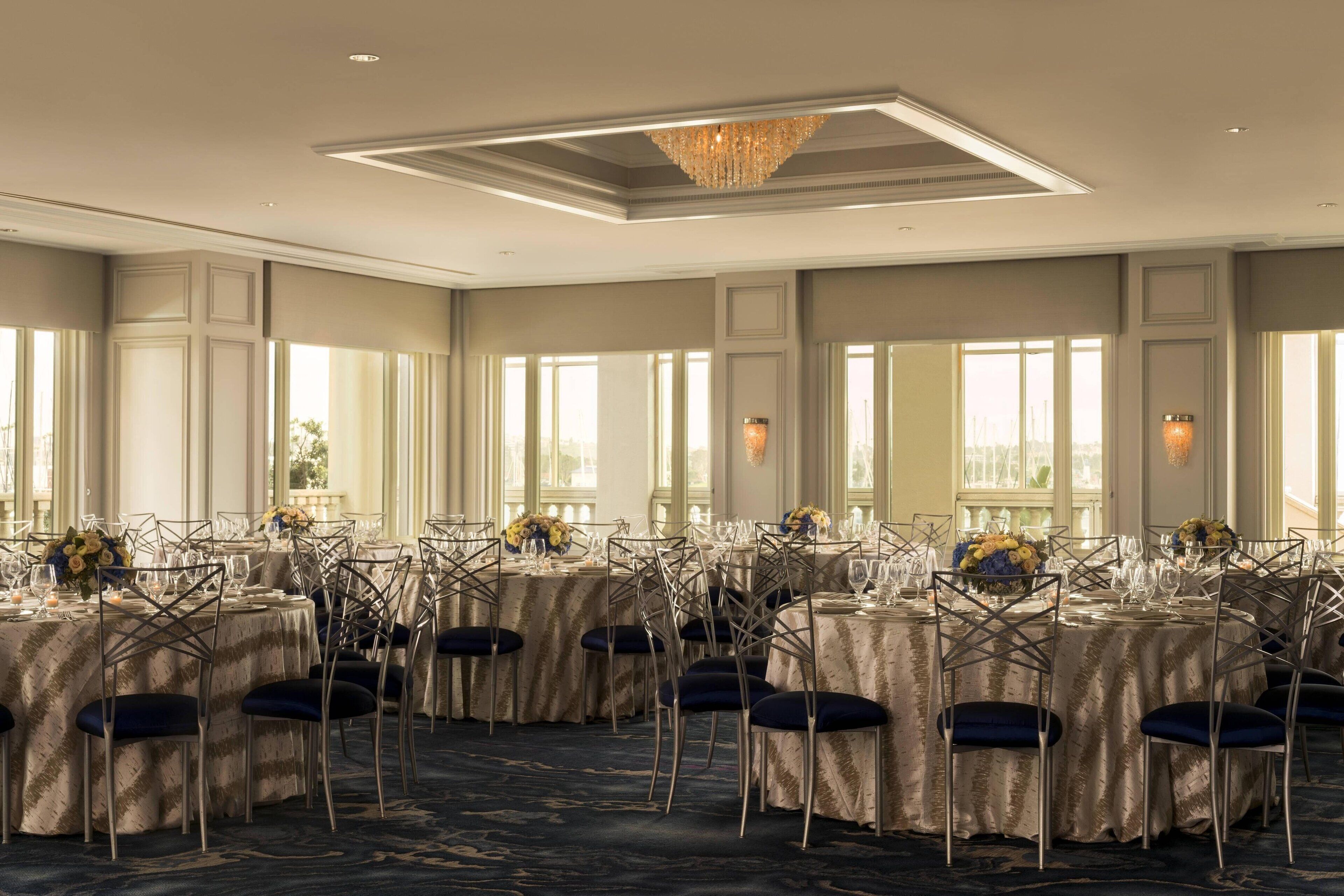 A banquet hall with round tables, chairs, and chandeliers.