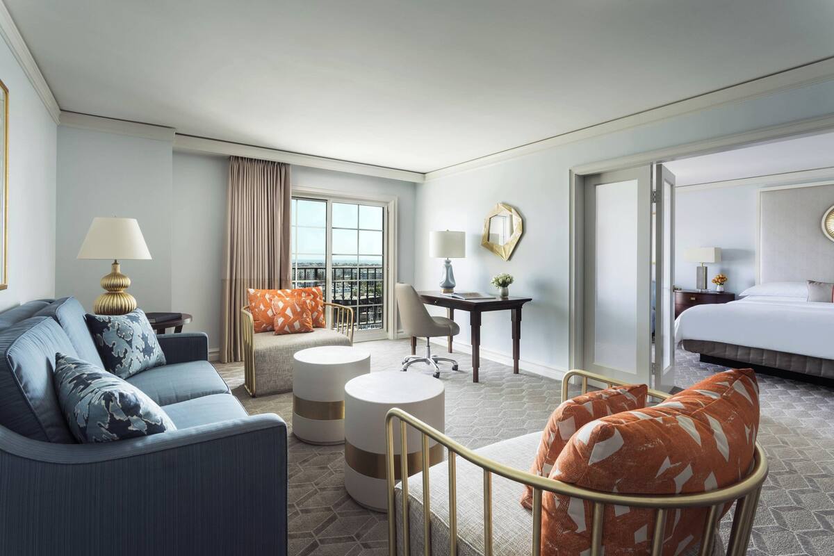 A hotel room with a sofa, armchair, round ottoman, desk, and bed.