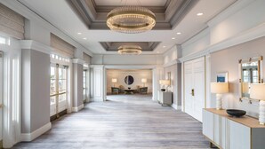 A spacious hallway with a patterned carpet, a chandelier, and a reception desk with a mirror and lamp. - The Ritz-Carlton, Marina del Rey (Marina del Rey)