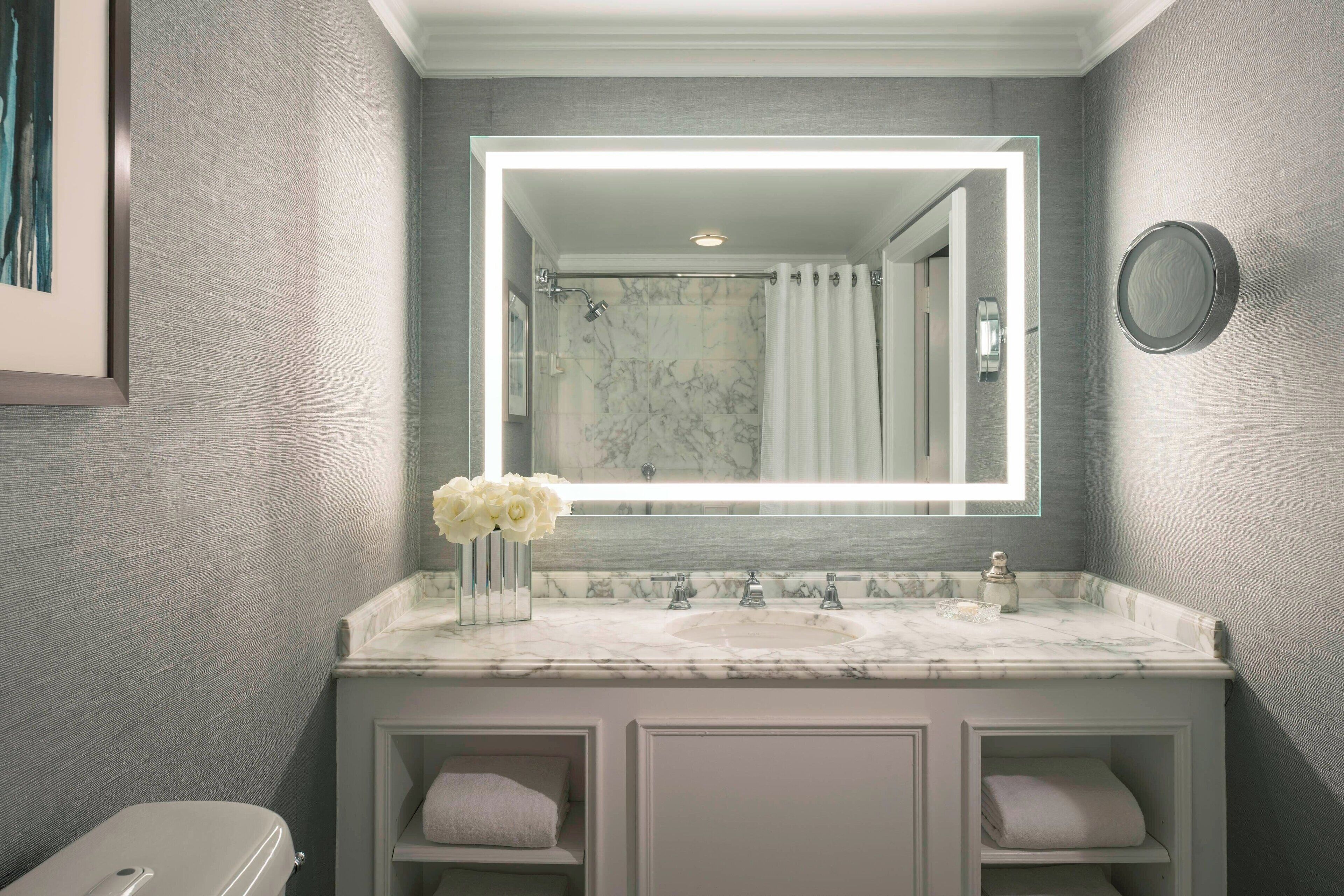 A bathroom with a marble sink, a large mirror, a shower, and a toilet.