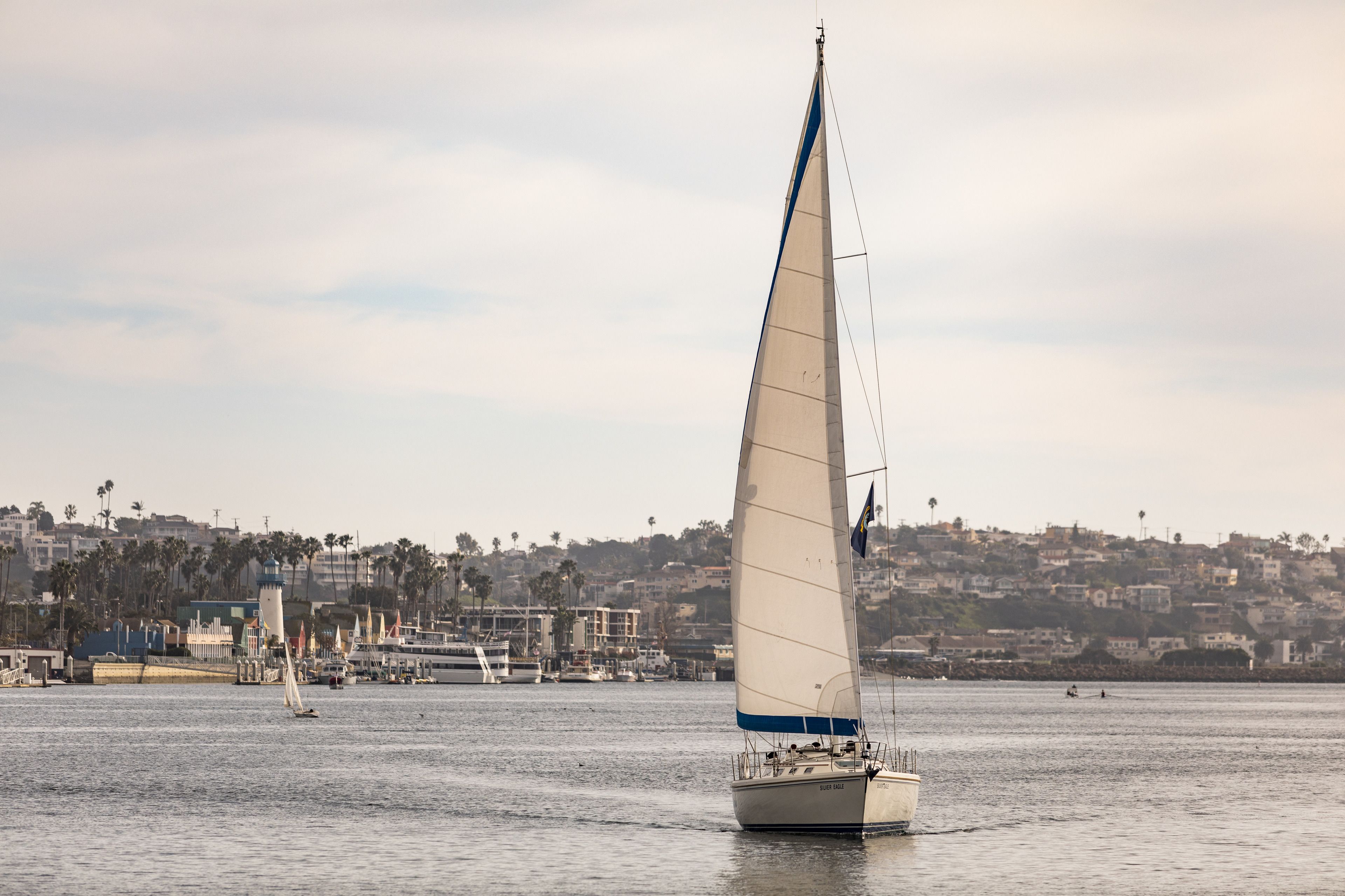 Un velero en aguas tranquilas, con un pueblo costero al fondo.
