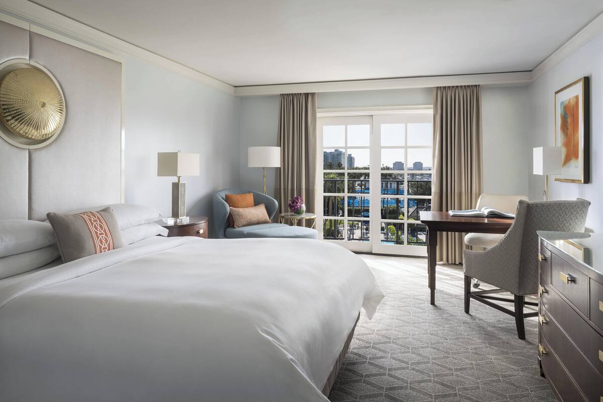 A hotel room with a large bed, a desk, a chair, and a view of the city through the window.