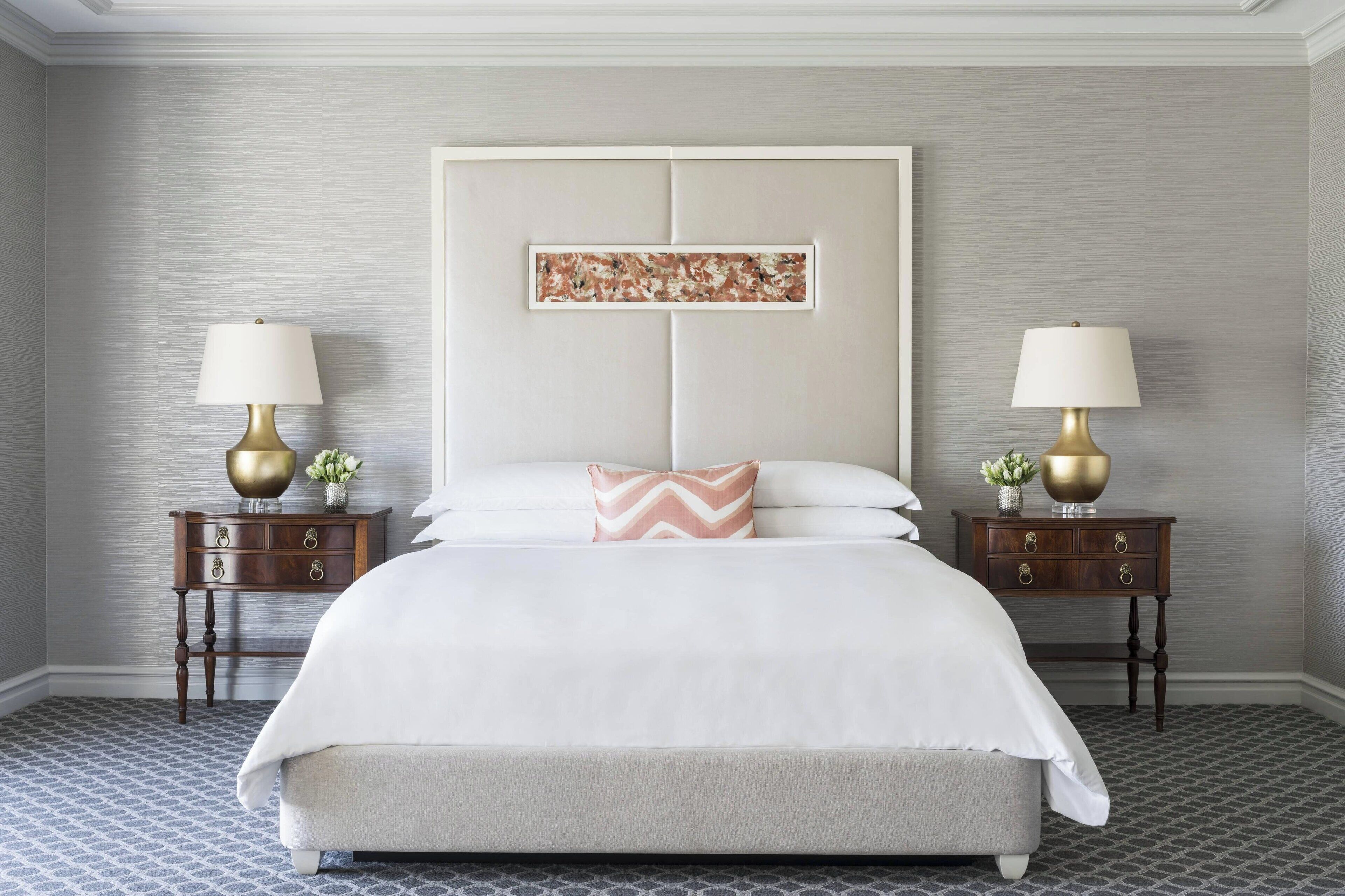 A neatly arranged bedroom with a large bed, two bedside tables with lamps, and a decorative piece above the bed.