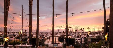 An outdoor seating area with tables and chairs, overlooking a marina with boats.