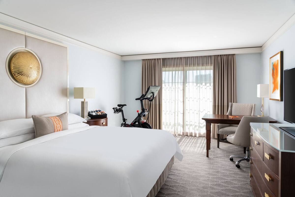 A hotel room with a large bed, a desk, a chair, a television, and a bicycle.