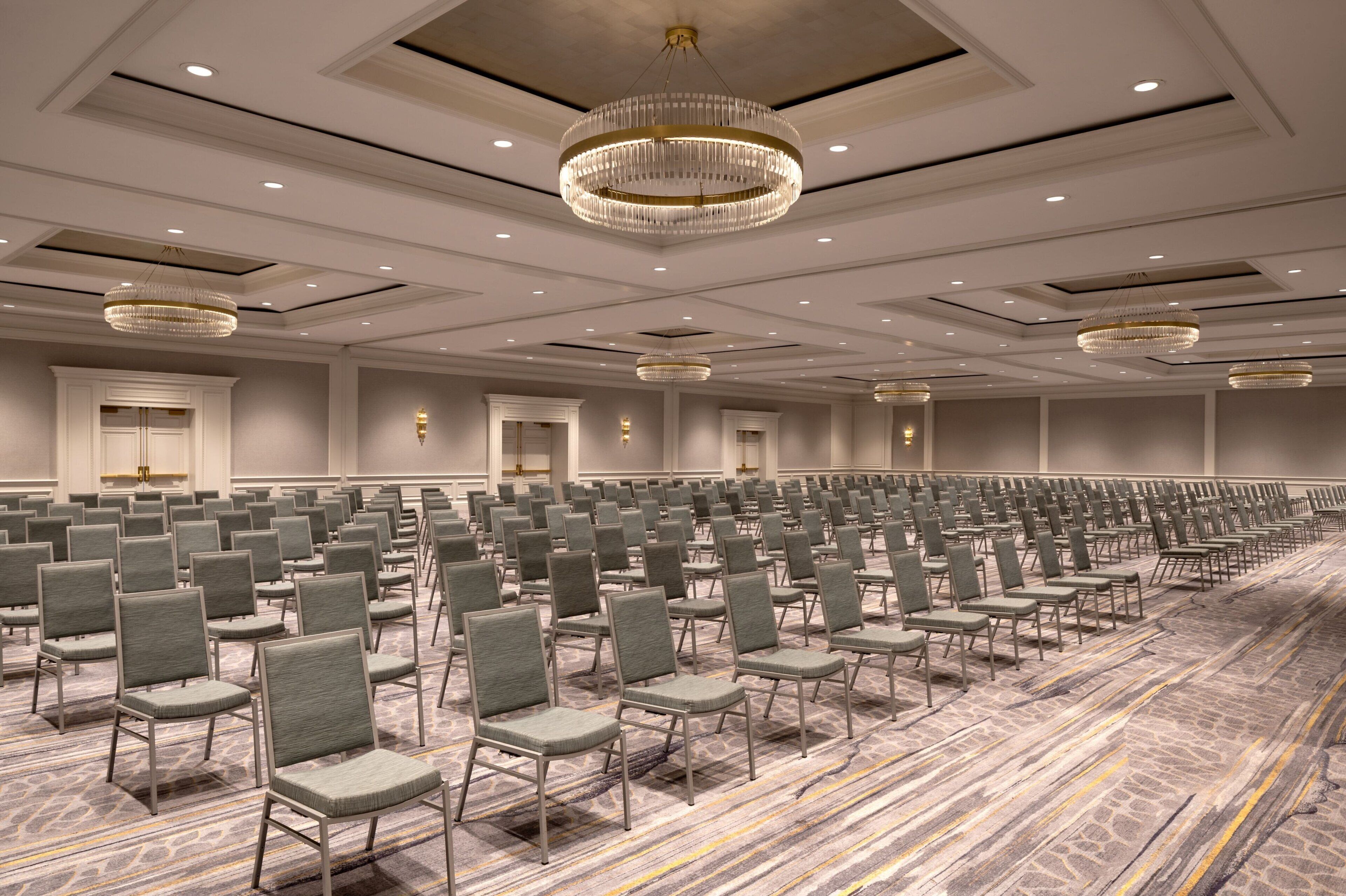 A large conference room with rows of chairs, chandeliers, and a patterned carpet.