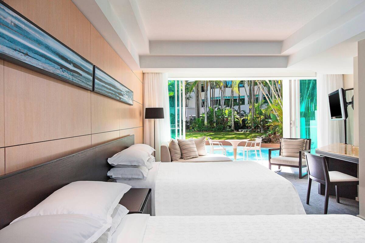 A hotel room with a large bed, a desk, and a view of a pool and greenery.