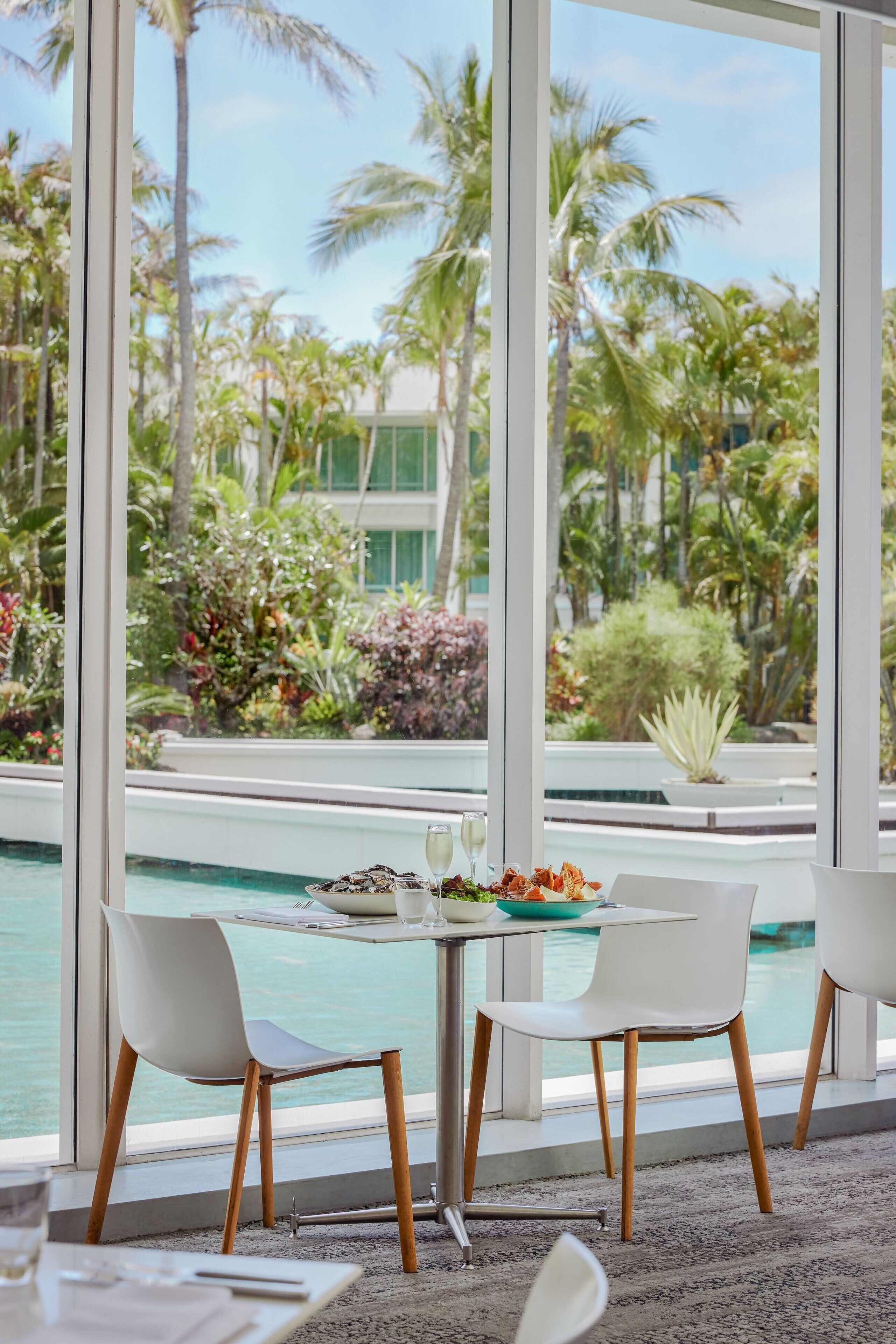 Un espace repas offrant une vue sur une piscine et une végétation tropicale.
