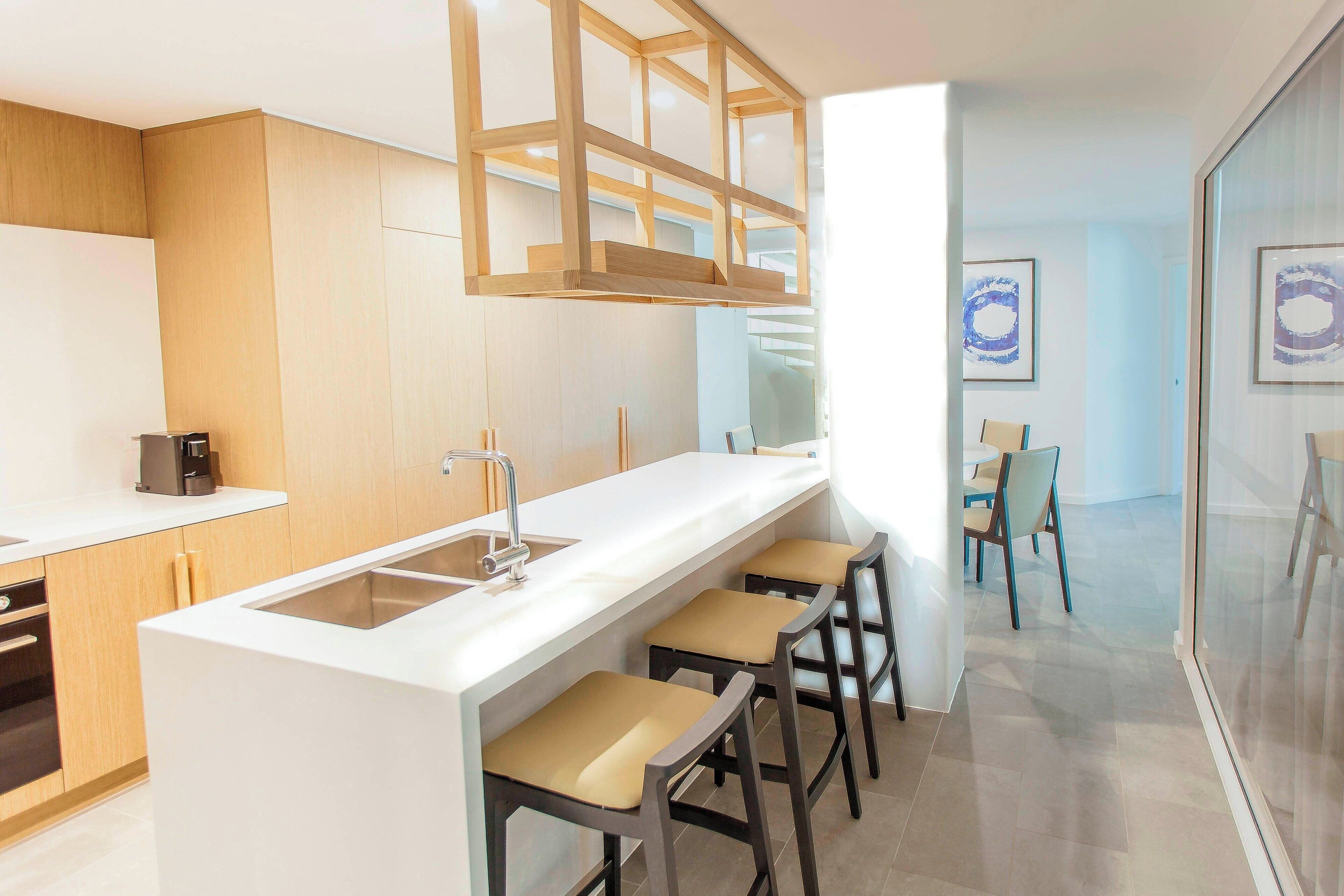 Uma cozinha moderna com uma ilha central, banquetas e um painel de vidro.