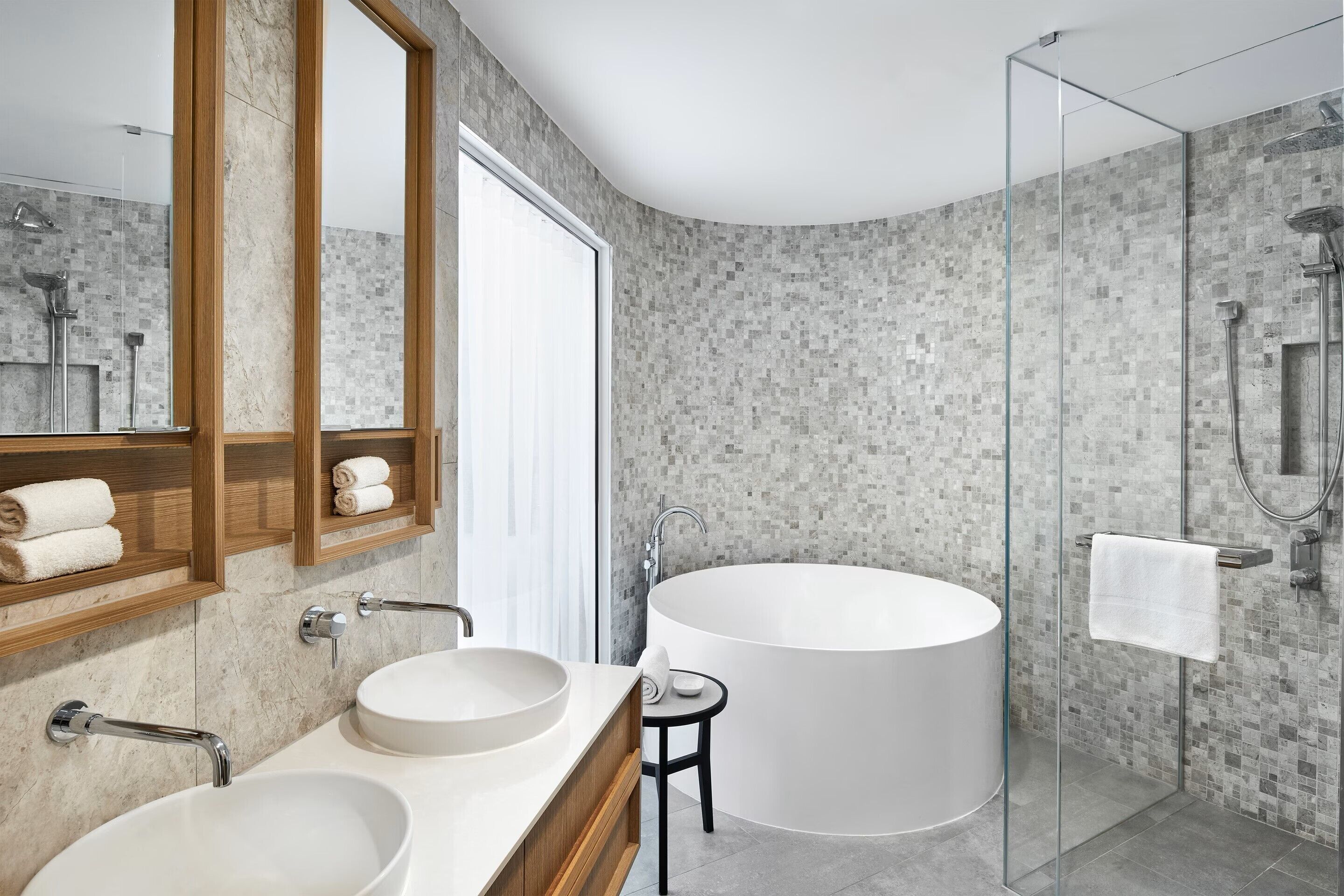A modern bathroom with a large bathtub, two sinks, a glass shower enclosure, and a mirror with a wooden frame.