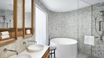 A modern bathroom with a large bathtub, two sinks, a glass shower enclosure, and a mirror with a wooden frame.
