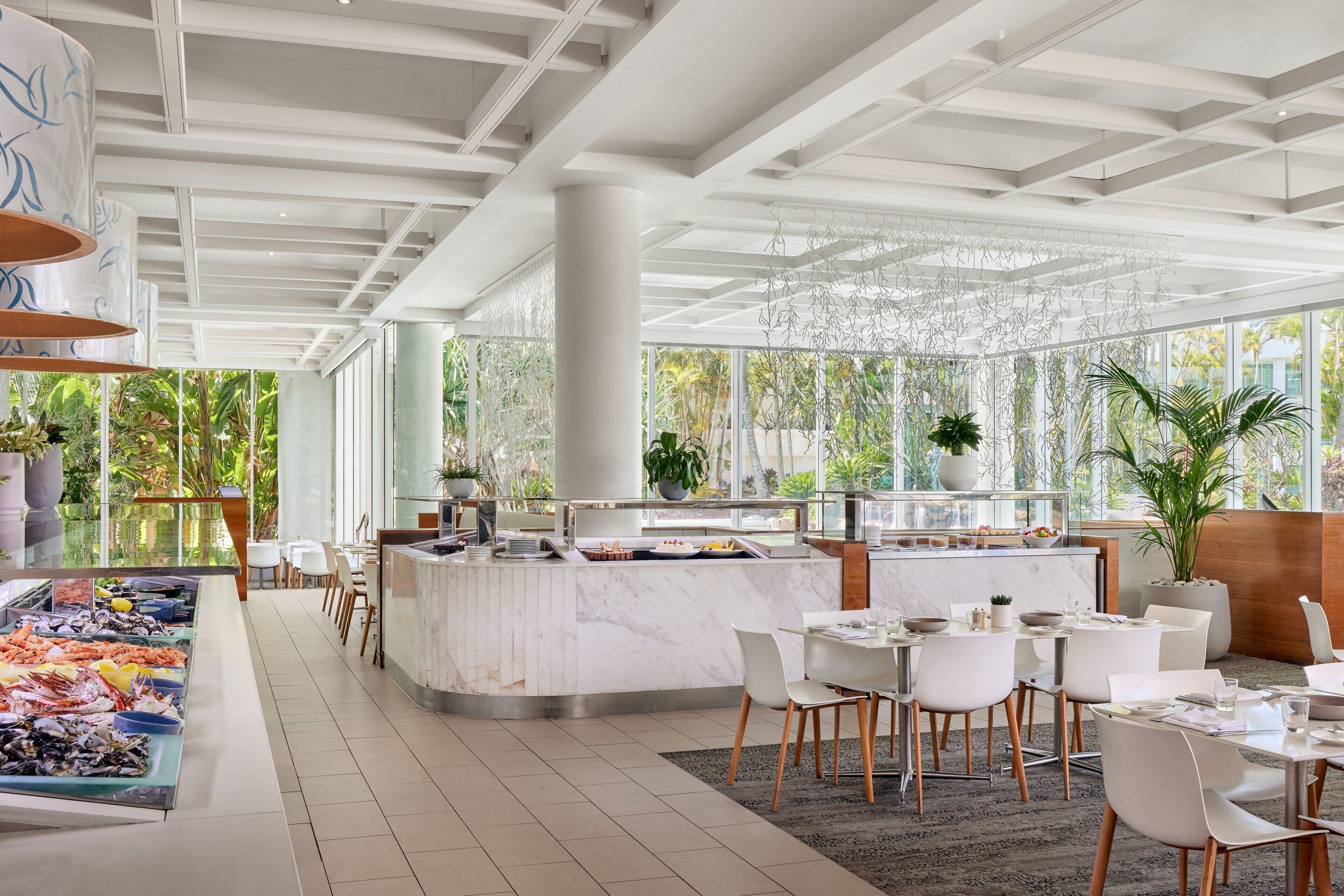 A modern restaurant with a central bar, white chairs, and a seafood display.