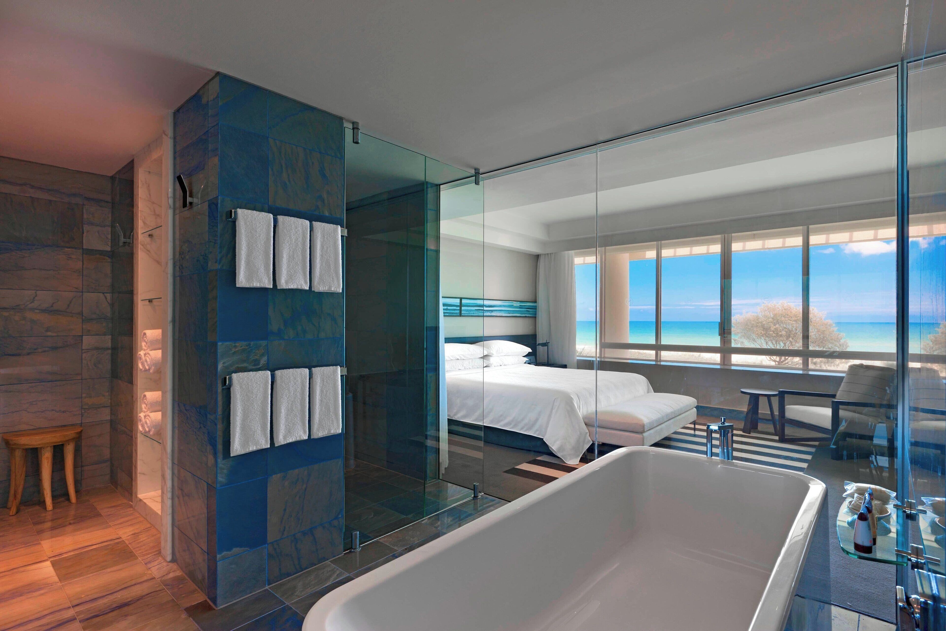 Een moderne badkamer met een douchecabine, een ruim bad en een bed met uitzicht op de oceaan.