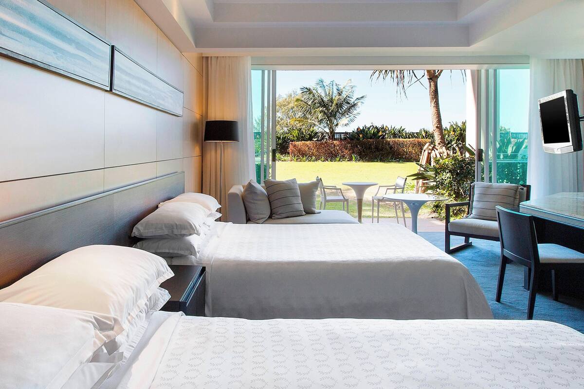 A hotel room with two beds, a desk, a chair, and a TV.