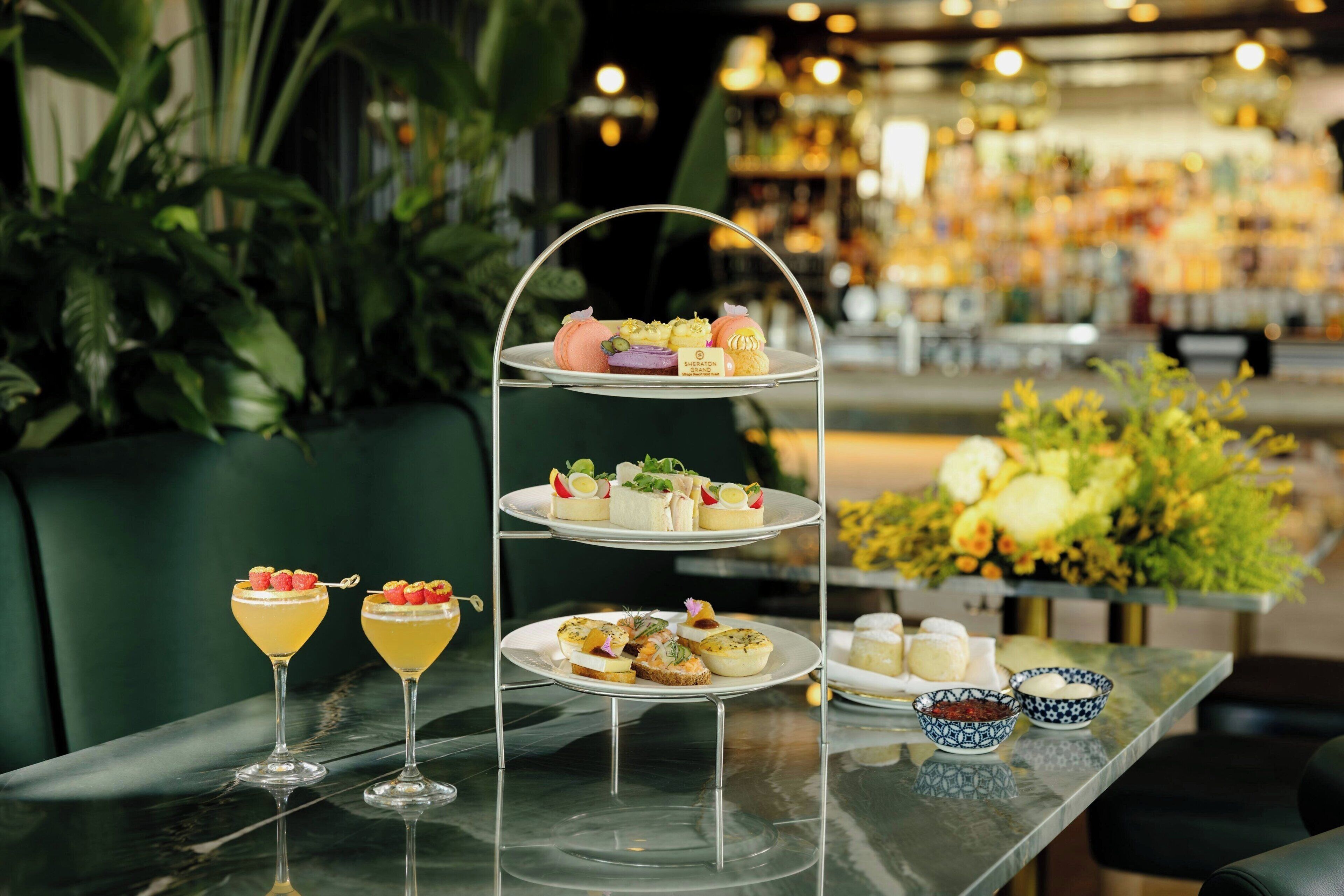 Un présentoir à trois niveaux, garni de diverses pâtisseries, et un verre de cocktail posés sur une table.