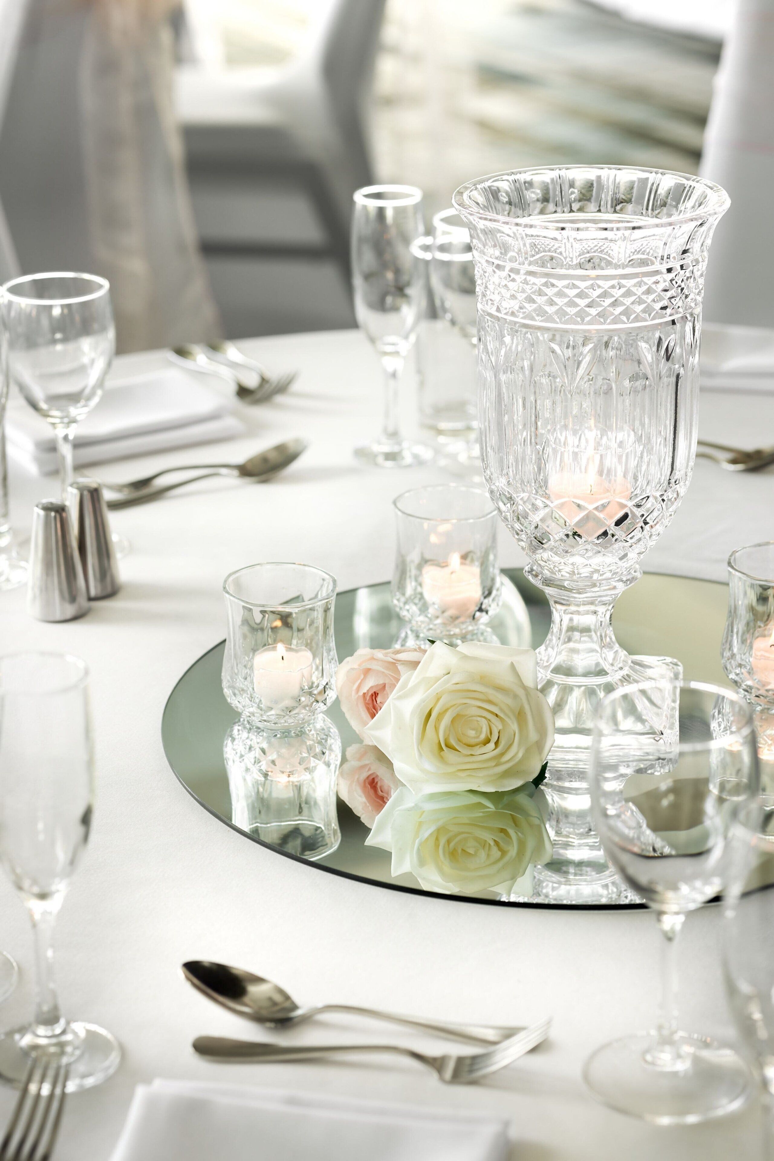 A table set with crystal glassware, candles, and a white rose.