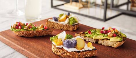 Three open-faced sandwiches on a wooden board with various toppings, a glass of a clear beverage, and a glass of a pale beverage in the background.