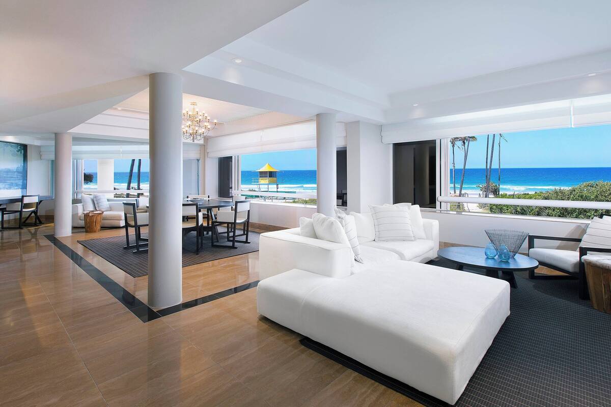 A spacious living area with a large white sofa, a round coffee table, and a view of the ocean.