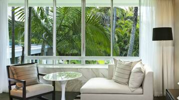 A modern hotel room with a large window, a white sofa, a small round table, and a chair.