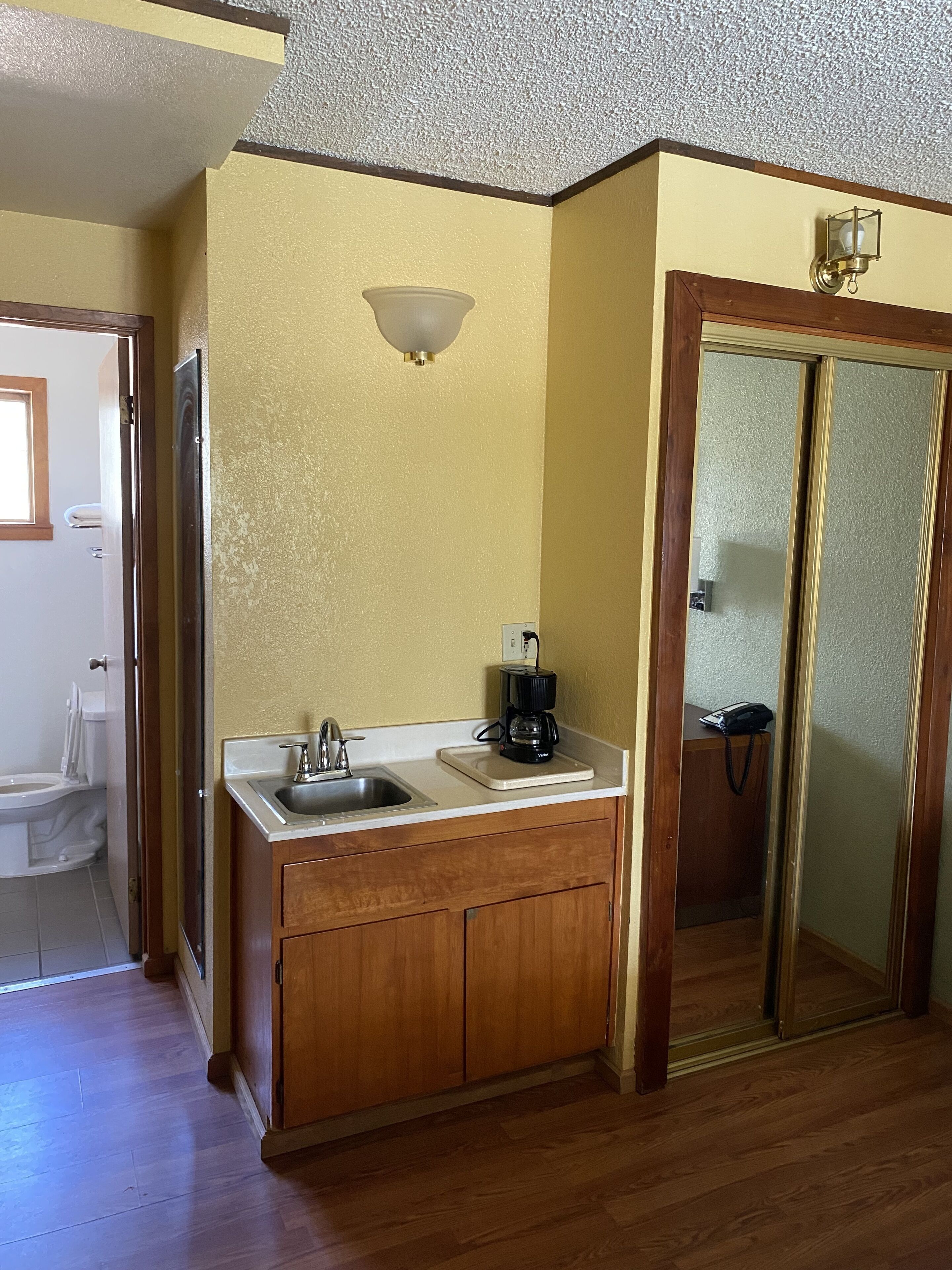 Una cocina compacta con pileta, cafetera, alacenas de madera y un espejo.