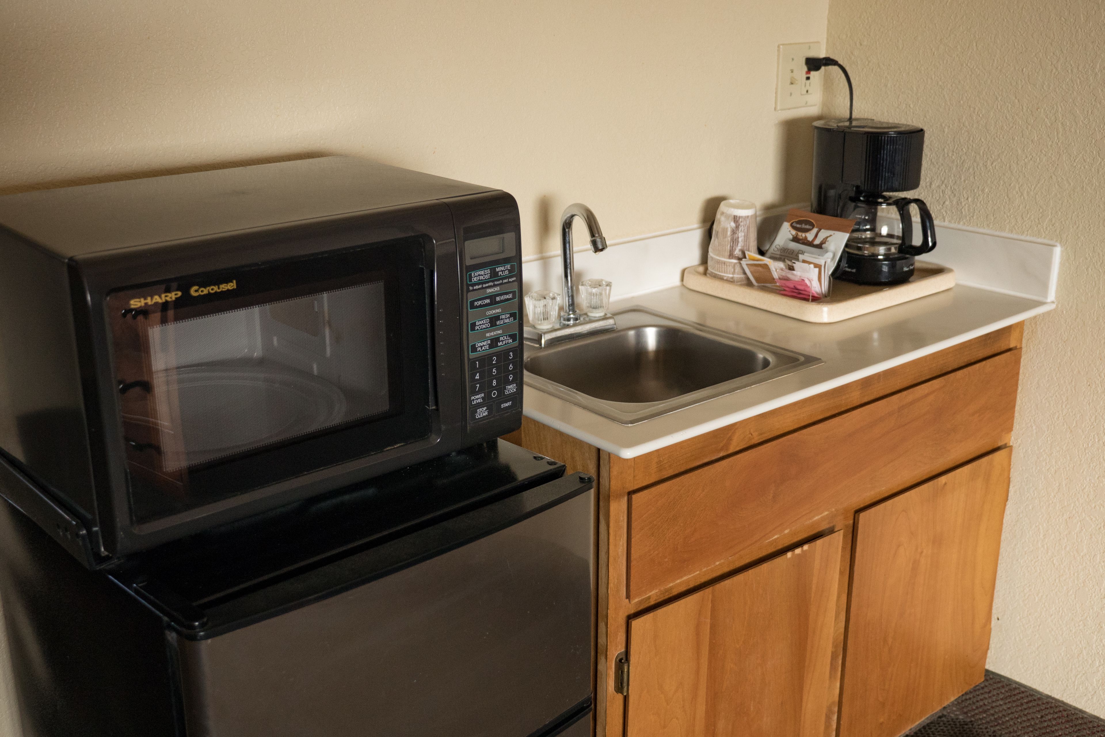 A kitchen with a black Sharp microwave, a coffee maker, and a sink.