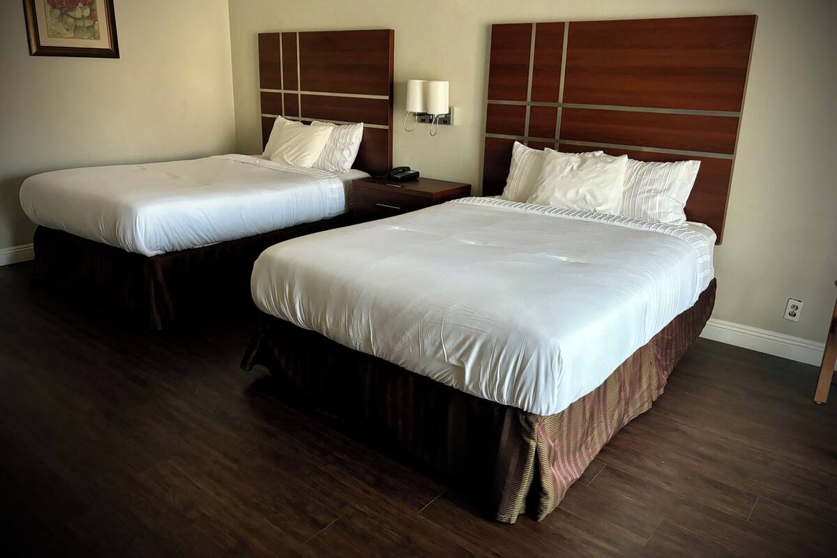 Two double beds with wooden headboards and white bedding in a hotel room.
