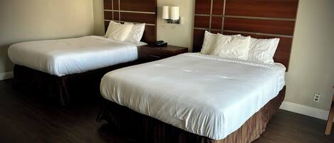 Two double beds with wooden headboards and white bedding in a hotel room.