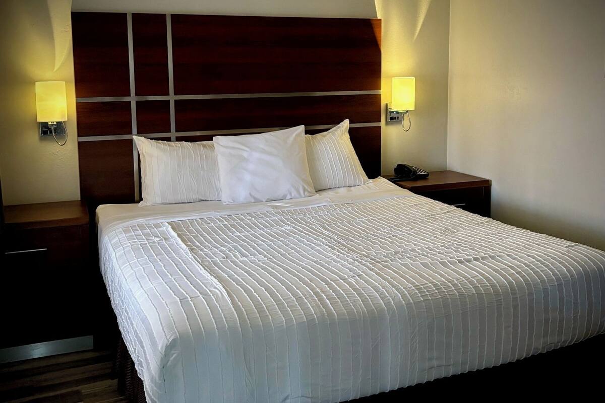 A neatly made bed with a headboard, two bedside lamps, and a wooden nightstand.