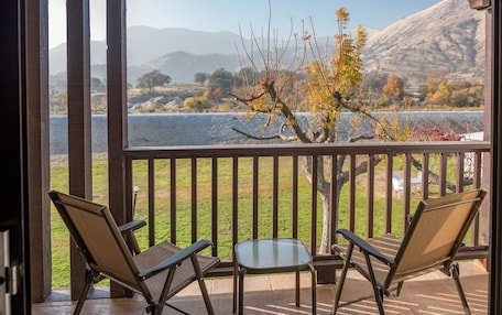 A balcony with two chairs and a small table, overlooking a grassy area and a body of water with mountains in the background.