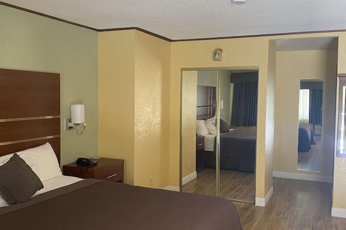 A hotel room with a large bed, a nightstand, a mirror, and a door leading to another room.
