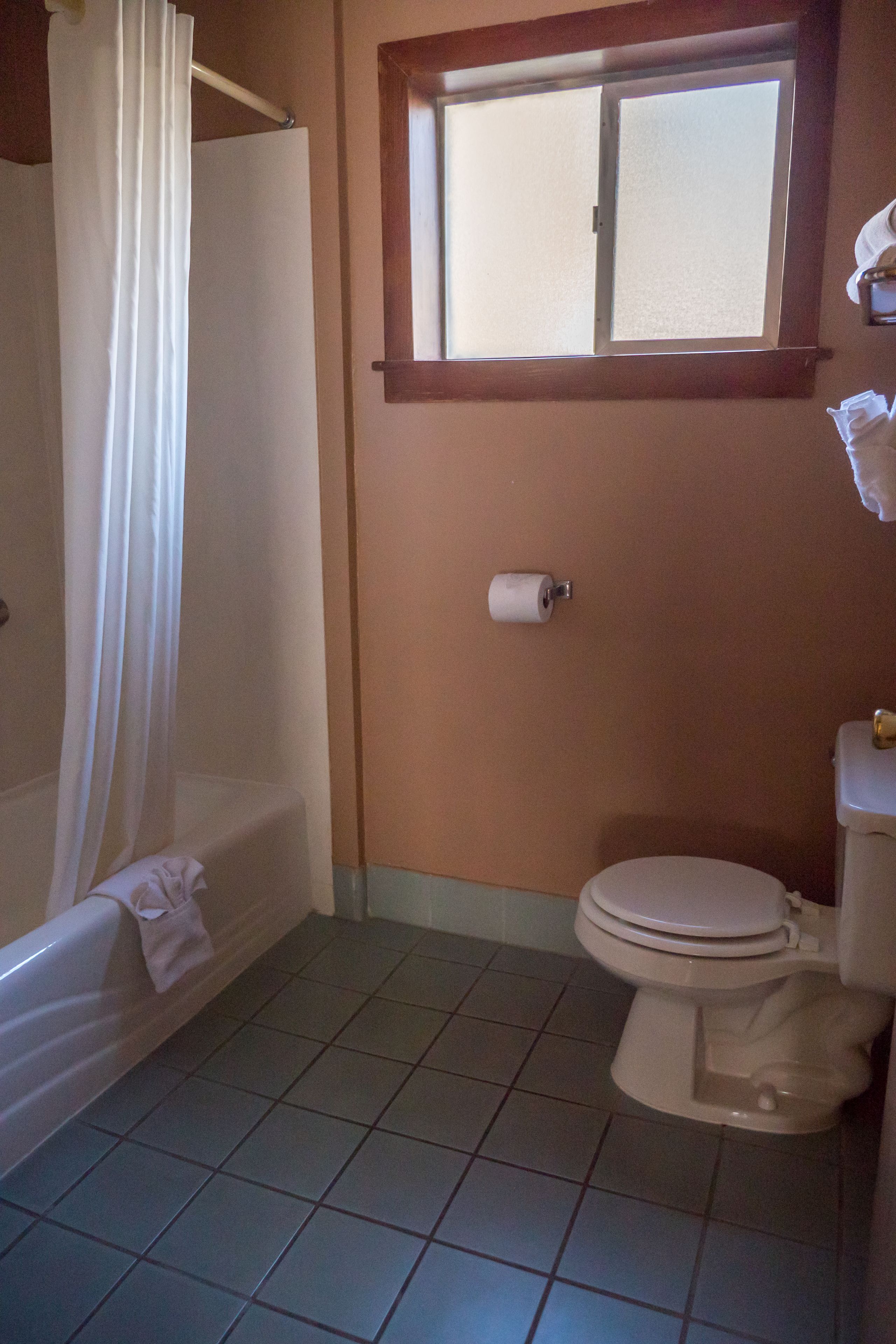 Une salle de bain avec une baignoire, des toilettes et une fenêtre située au-dessus des toilettes.