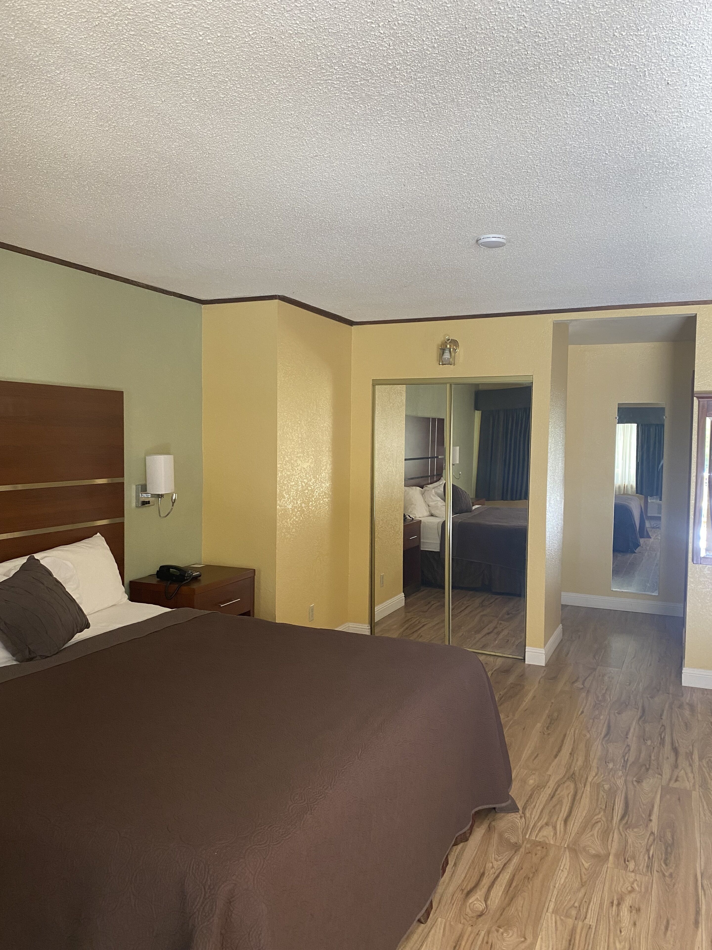Habitación de hotel con una cama grande, una mesita de noche con lámpara, teléfono y espejo.
