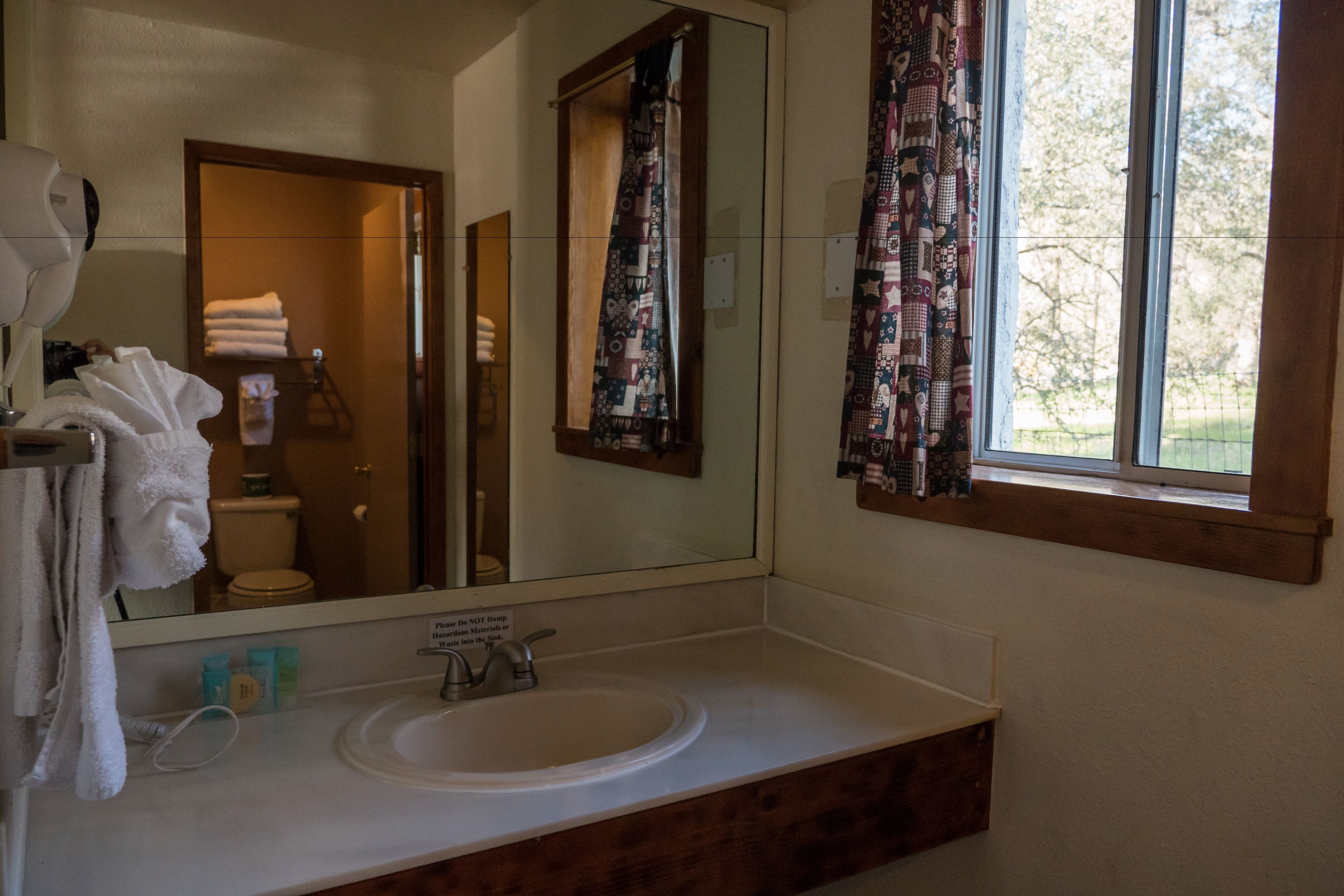 A bathroom with a large mirror, a sink, and a window with curtains.