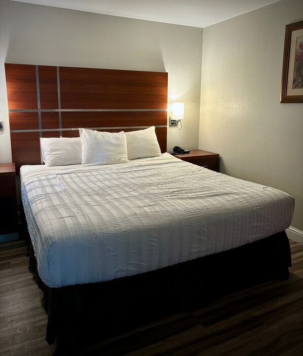 A hotel room with a large bed, a wooden headboard, a bedside table with a lamp, and a framed picture on the wall.