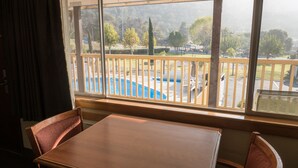 A room with a wooden table and chairs, a window with a view of a pool and trees.