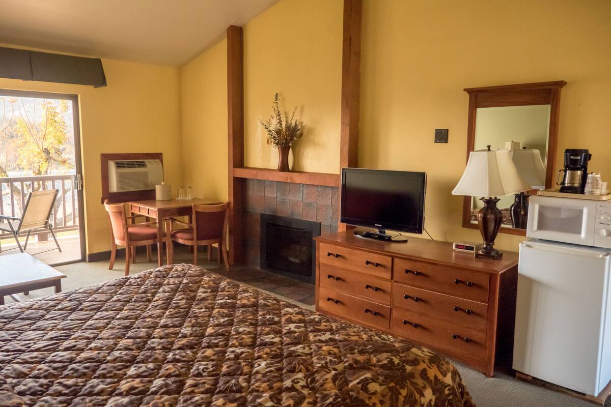 A hotel room with a bed, a TV, a fireplace, a desk, and a dining area.