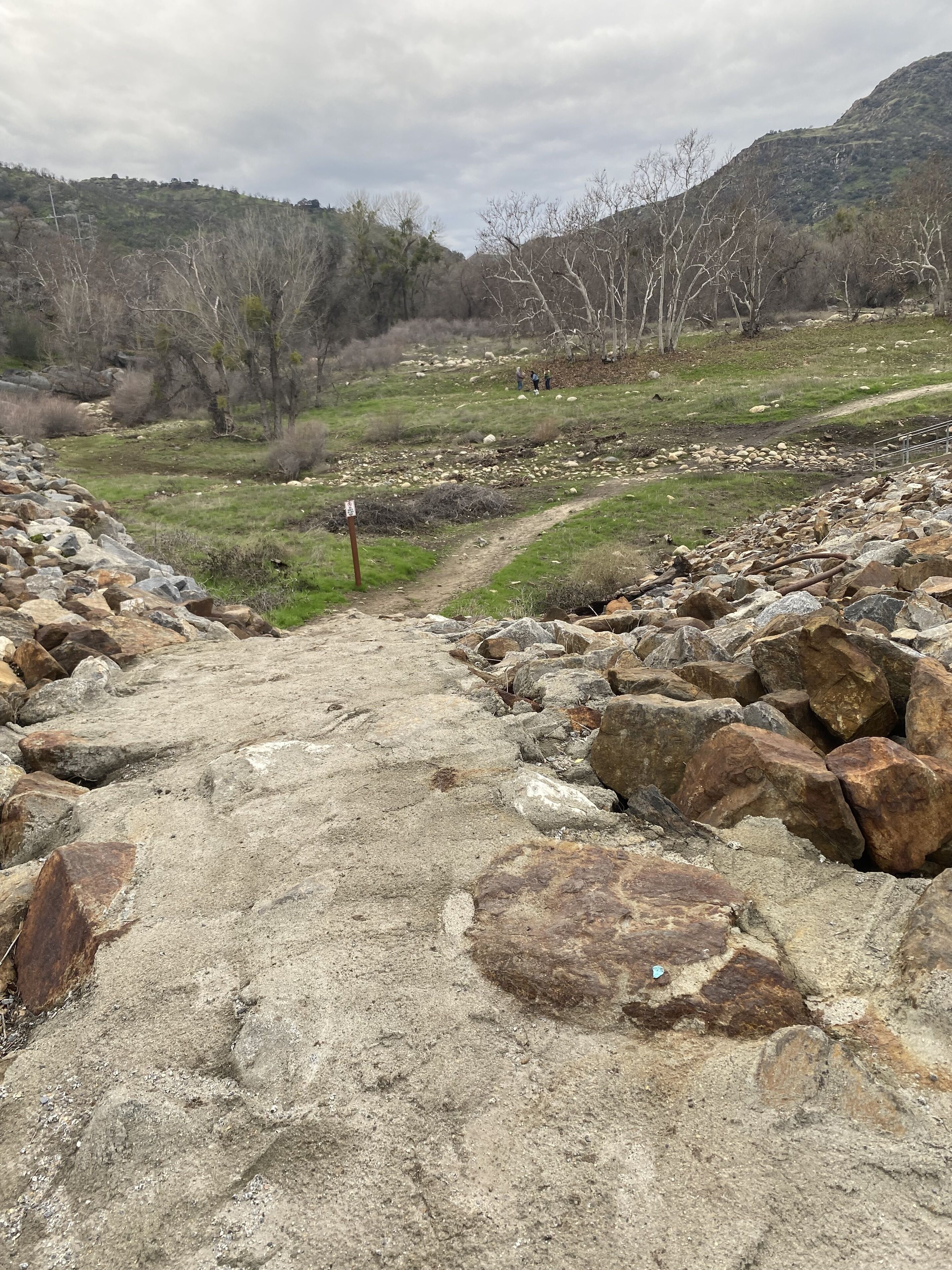 A rocky path leading into a hilly landscape with sparse vegetation and a few people in the distance.