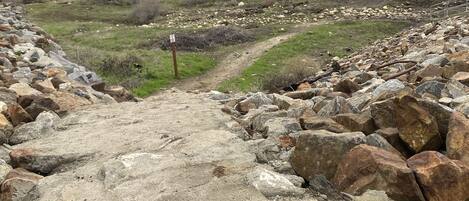A rocky path leading into a hilly landscape with sparse vegetation and a few people in the distance.