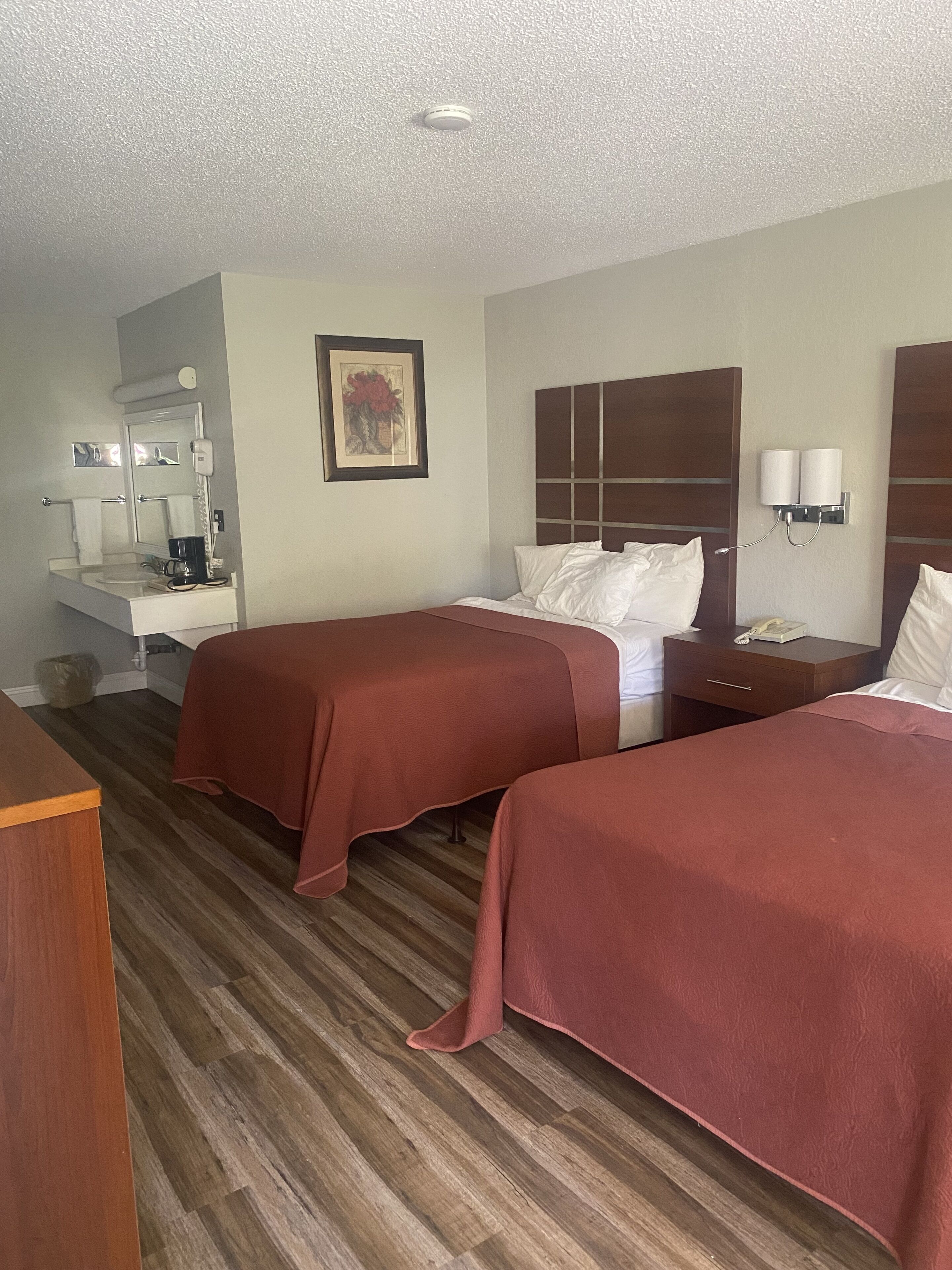 A hotel room with two beds, a desk with a mirror, a coffee maker, and a framed picture on the wall.