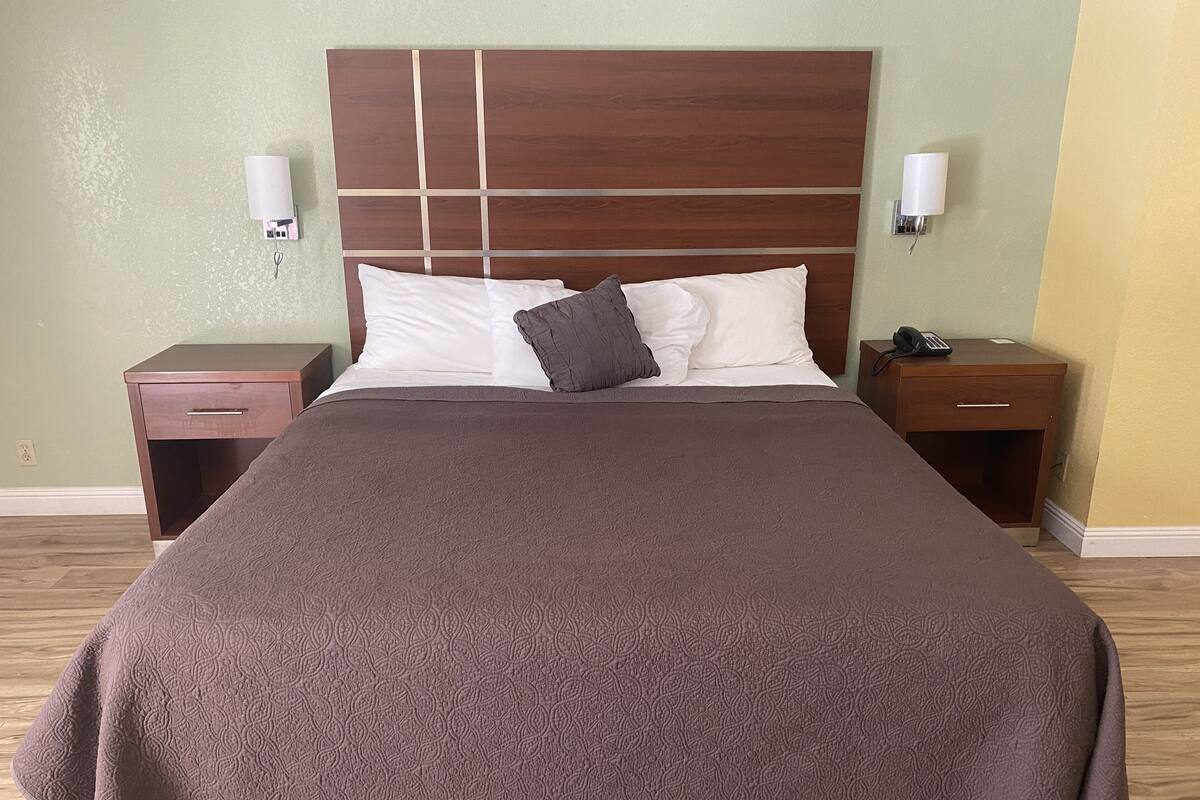 A neatly made bed with a brown bedspread and two pillows, flanked by wooden nightstands with lamps and a phone.
