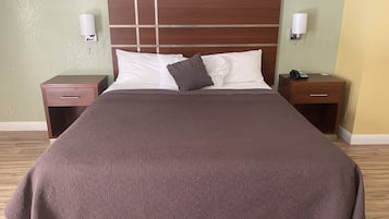 Ein ordentlich bezogenes Bett mit brauner Tagesdecke und zwei Kissen, flankiert von Nachttischen aus Holz mit Lampen und einem Telefon.