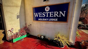 A sign for Western Holiday Lodge with a red carpet entrance and potted plants.