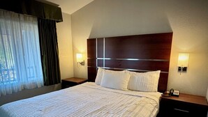Una habitación de hotel con una cama grande, dos mesitas de noche y una ventana con cortinas.