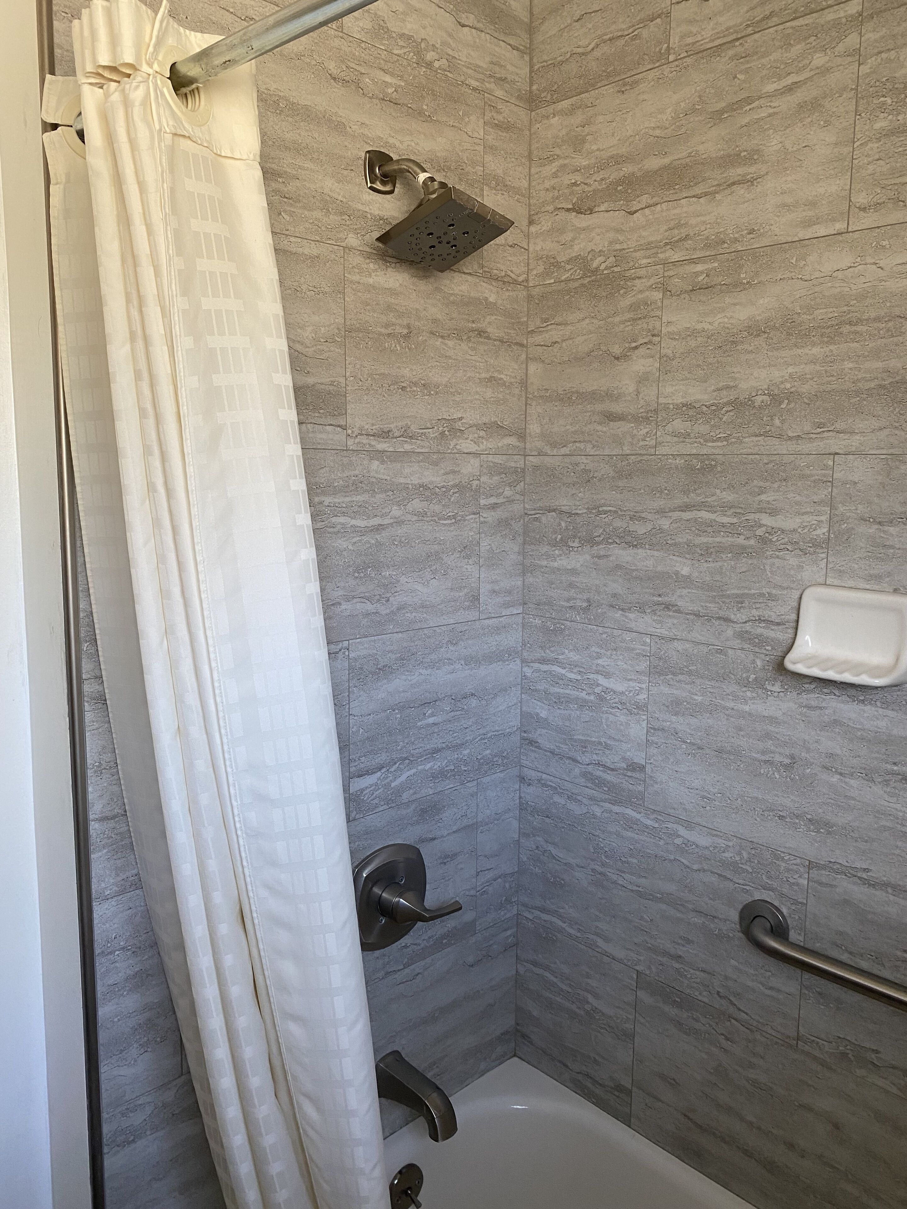 A modern shower area with a glass door, a handheld showerhead, and a handheld faucet.